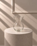 Jarrón Cristal Clásico transparente con silueta curvada y boca abierta, sobre pedestal de piedra