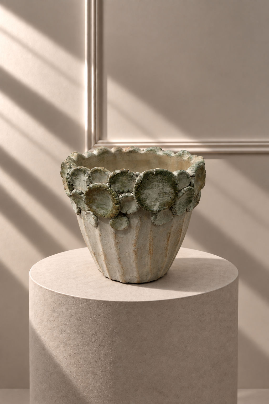 Jarrón Jardín Gris sobre pedestal, con acabado envejecido y borde decorativo de formas redondeadas en relieve.