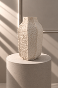 Jarrón Prisma Marfil con silueta facetada y relieve texturizado, sobre pedestal de piedra