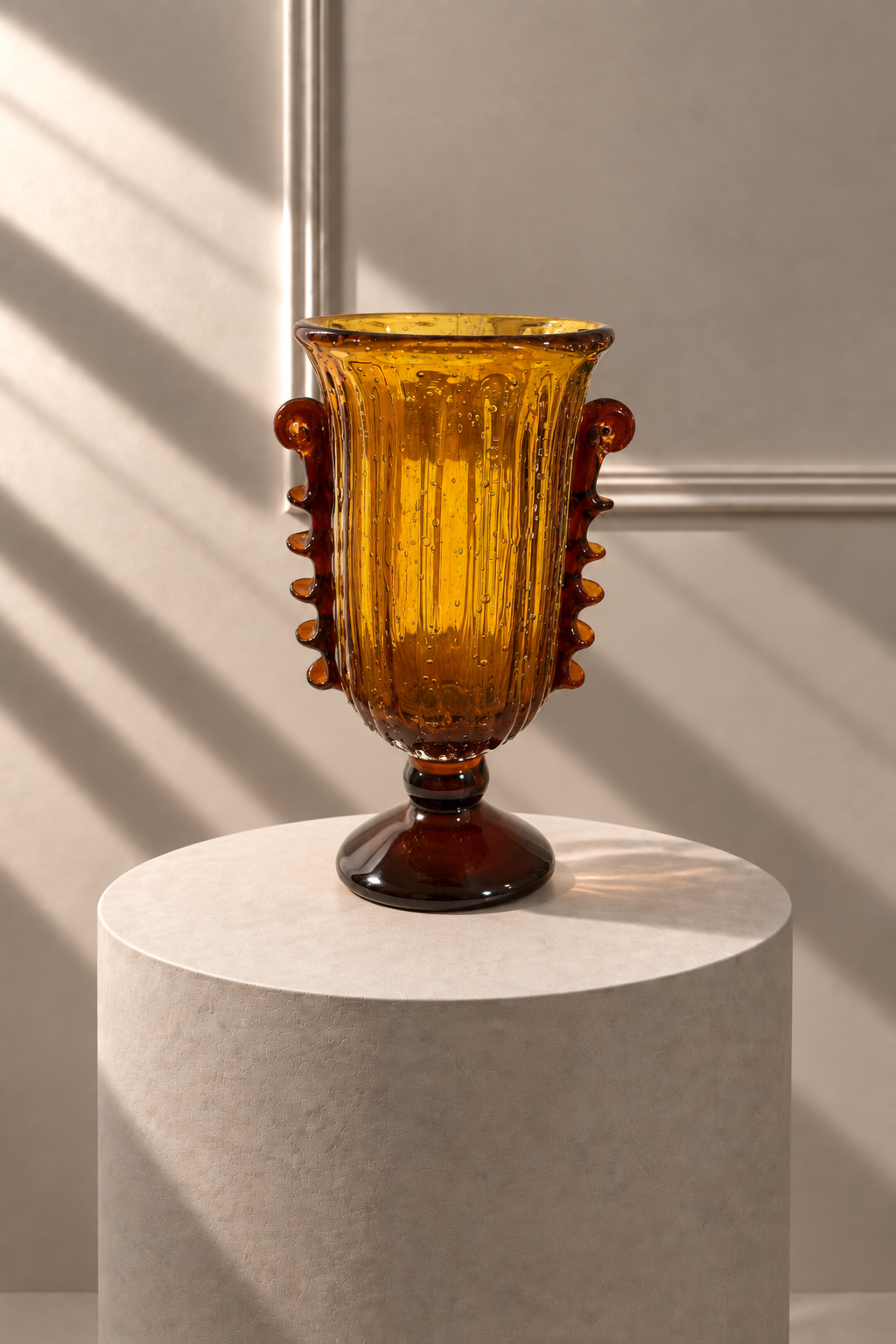 Jarrón Ámbar Majestad de vidrio ámbar con asas ornamentales, sobre pedestal de piedra