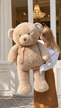 Oso de peluche gigante beige de 125 cm con lazo, sostenido por una mujer