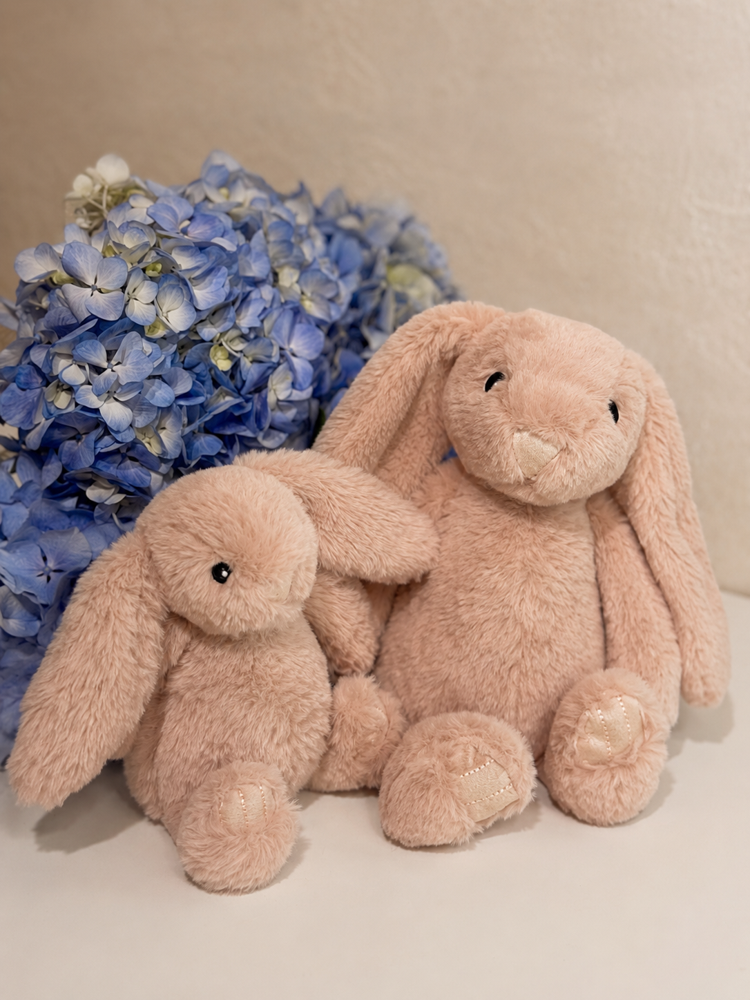 Conejos de peluche rosa en tamaño pequeño y grande junto a hortensias azules