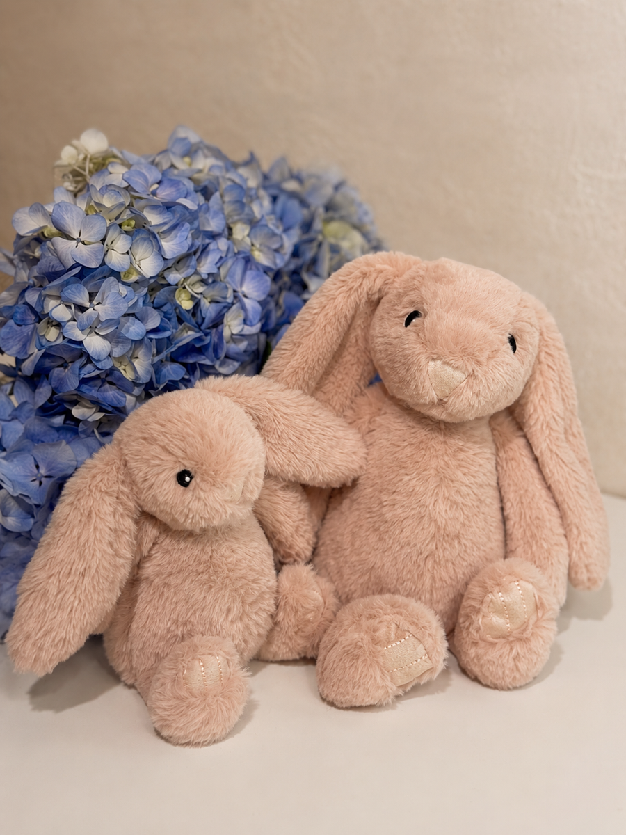 Conejos de peluche rosa en tamaño pequeño y grande junto a hortensias azules