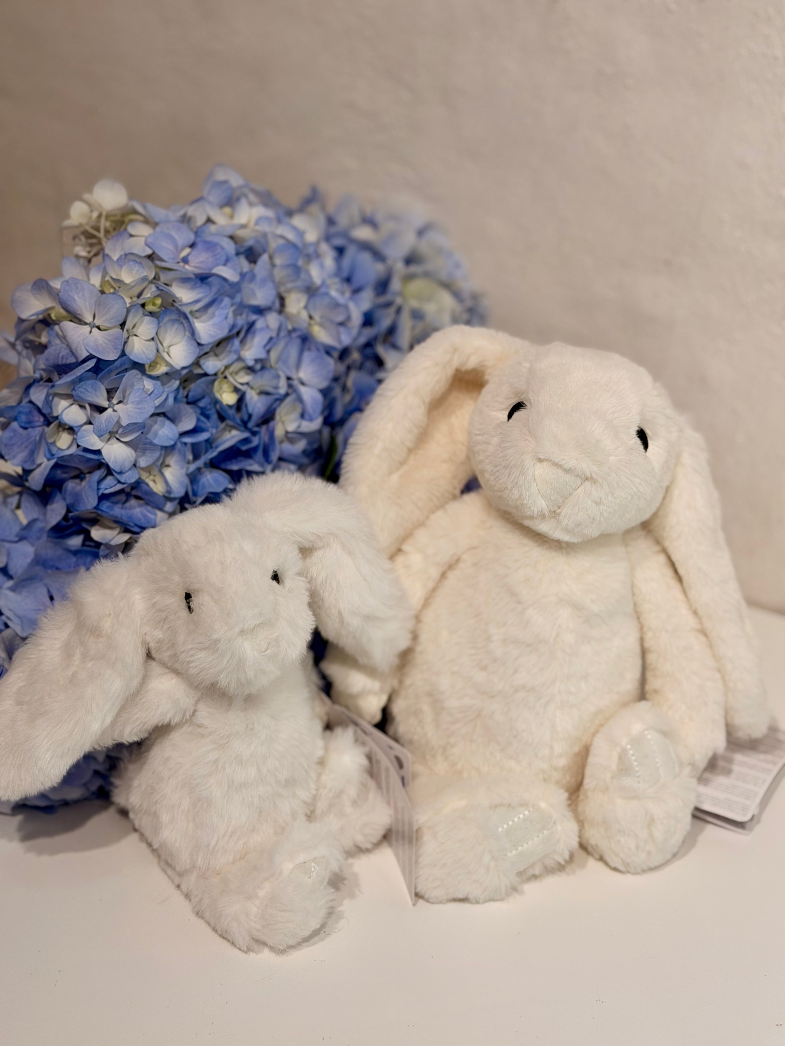 Conejos de peluche blanco en tamaño pequeño y grande junto a hortensias azules
